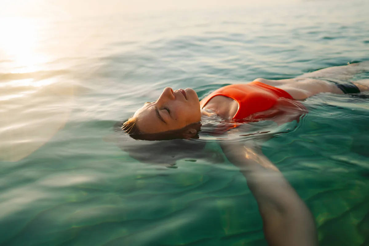 Frau schwimmt entspannt im Meer bei Sonnenuntergang