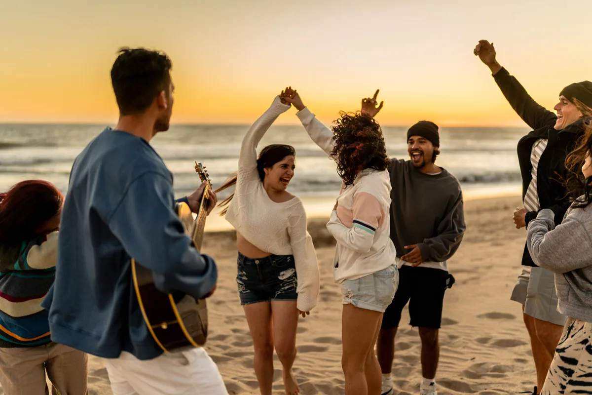 Junge Menschen tanzen am Strand bei Sonnenuntergang